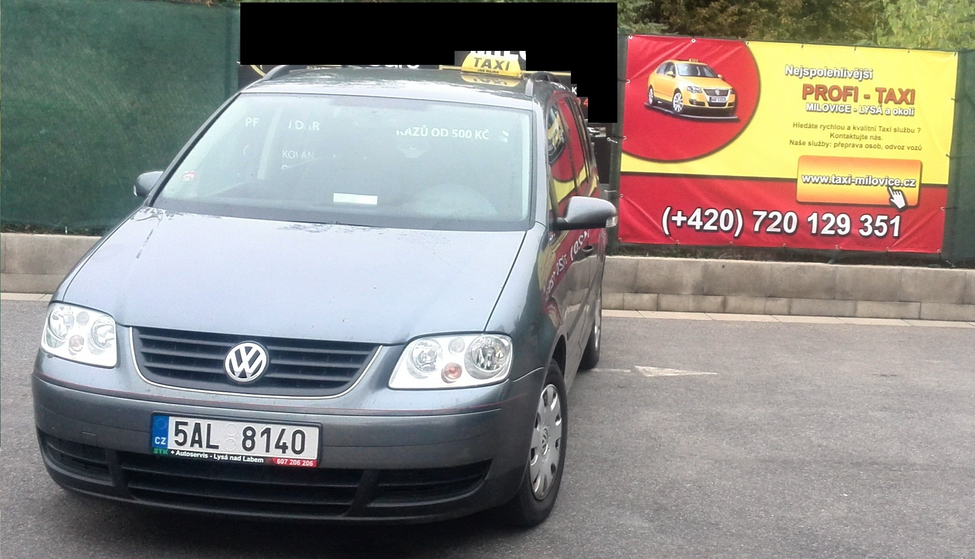 Vozidlo Profi Taxi VW Touran u reklamního banneru v Milovicích